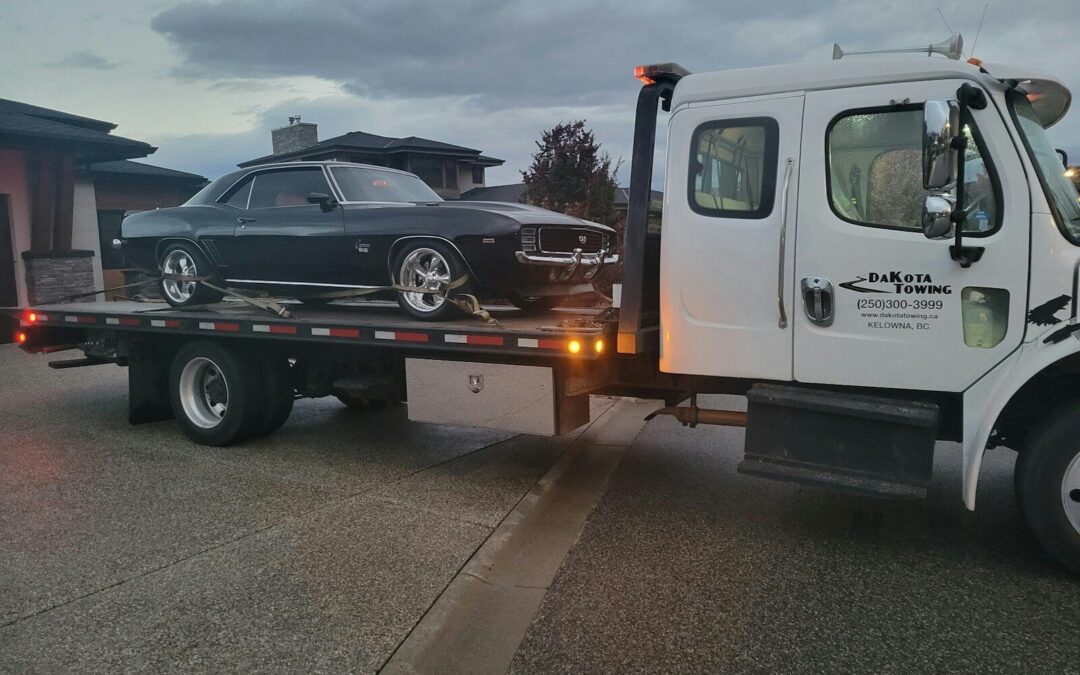 A black classic car loaded onto a tow truck.